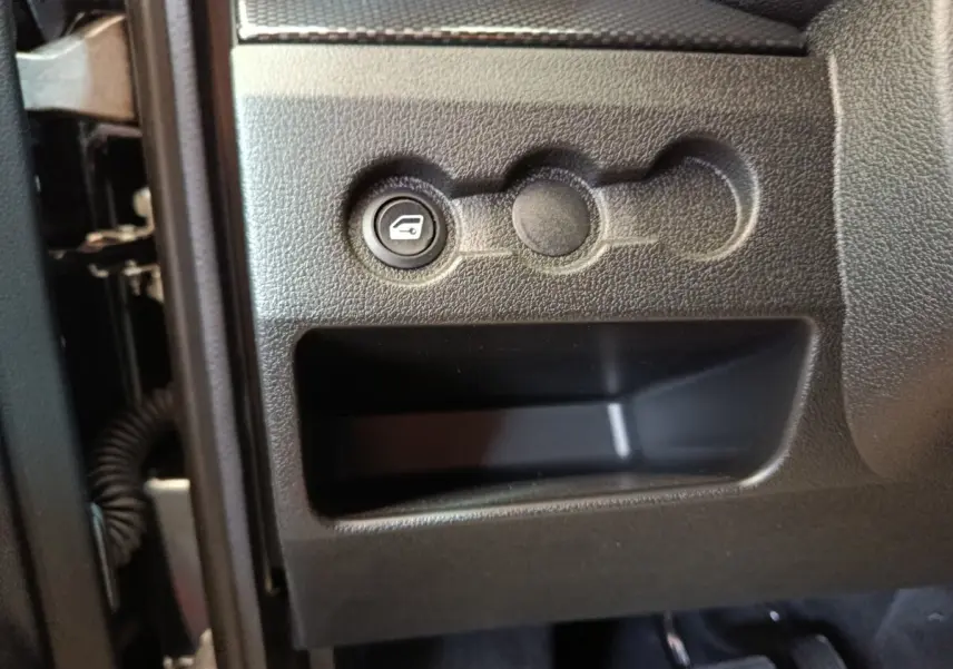 Détail intérieur montrant le bouton d'ouverture du coffre sur le tableau de bord noir côté conducteur de l'AIXAM Ambition 2026.
