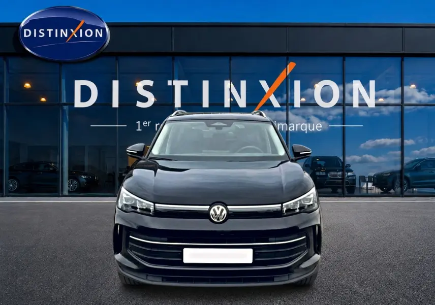 Vue frontale d'un Volkswagen Tiguan noir 2025 avec calandre large et logo VW centré devant un showroom Distinxion.