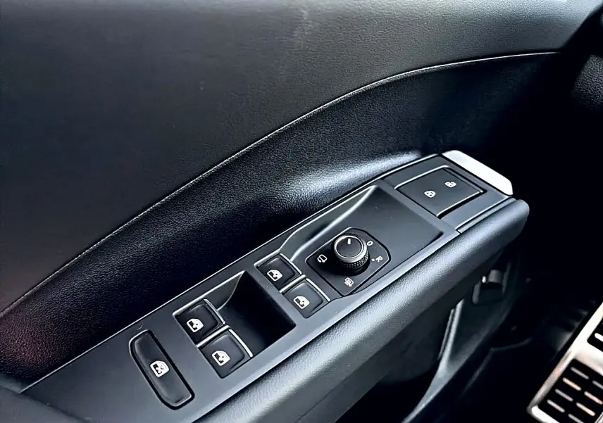 Gros plan sur la commande des vitres et rétroviseurs côté conducteur intérieur noir du Volkswagen T-Roc bleu céleste 2026.