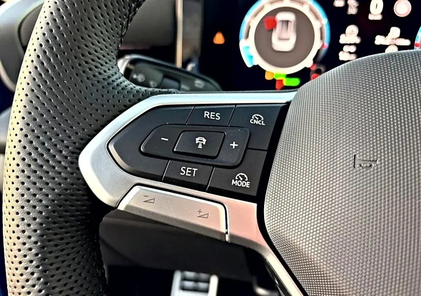 Gros plan sur les commandes multifonctions noires et argent du volant sport perforé du Volkswagen T-Roc bleu céleste 2026.