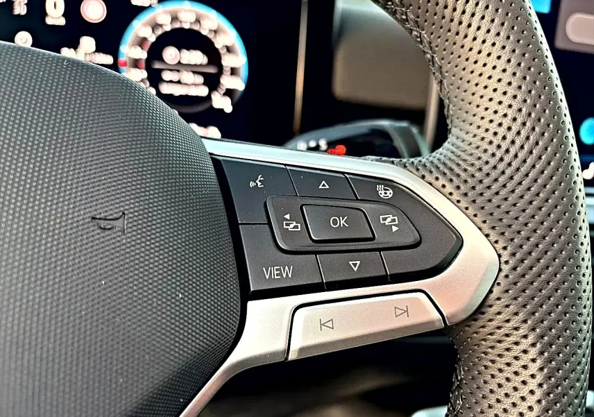 Gros plan sur le volant cuir perforé du Volkswagen T-Roc 2026 avec commandes multifonctions et affichage digital flou.