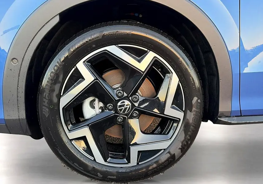 Gros plan sur la roue avant gauche d’un Volkswagen T-Roc bleu céleste avec jante alu noire et argentée au design géométrique.