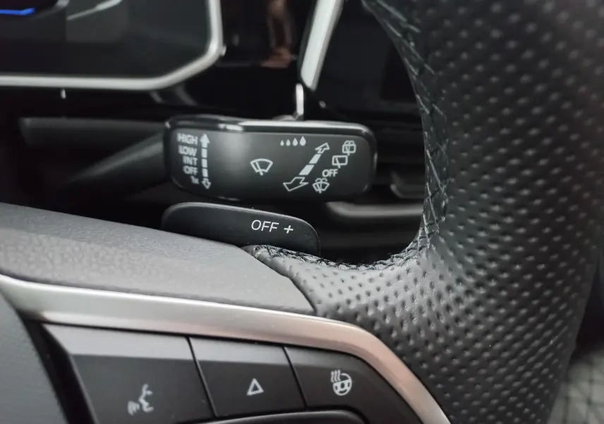 Gros plan sur le volant noir perforé du Volkswagen T-Roc blanc, avec commandes de régulateur et volant chauffant visibles.