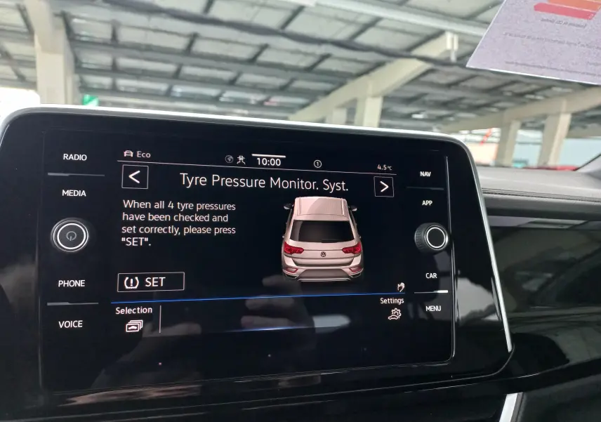 Écran central affichant le système de surveillance de pression des pneus du Volkswagen T-Roc blanc, vue arrière stylisée.