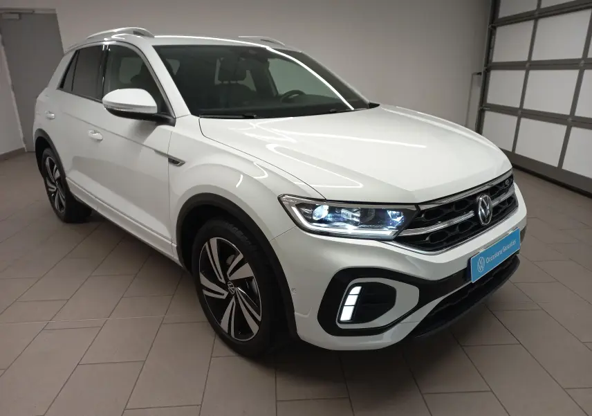 Volkswagen T-Roc blanc pur en vue 3/4 avant droit, phares LED allumés et jantes R-Line distinctives.