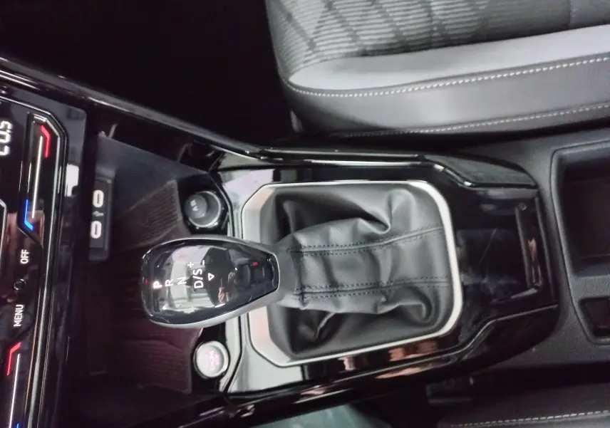 Vue rapprochée de la console centrale du Volkswagen T-Roc blanc, mettant en valeur le levier de vitesse automatique et le siège tissu gris.