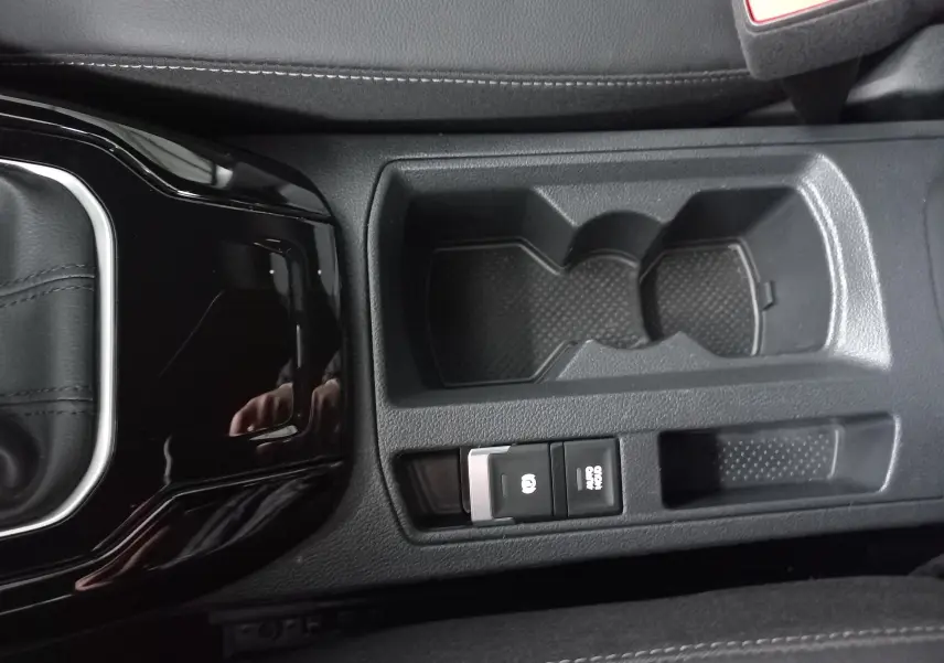 Vue rapprochée de la console centrale noire du Volkswagen T-Roc 1.5 TSI R-Line avec porte-gobelets et frein à main électronique.