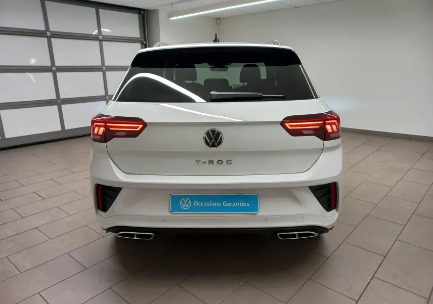 Vue arrière d'un Volkswagen T-Roc blanc pur 2025 avec feux LED allumés et double sortie d'échappement chromée.