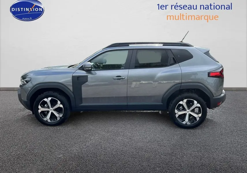 Profil droit du Dacia Duster 2025 gris schiste avec jantes alu et barres de toit noires visibles.