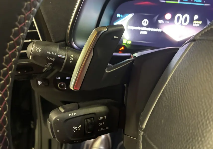 Gros plan sur la commande de régulateur de vitesse et commodo d’éclairage à gauche du volant dans un DS7 gris 2024.