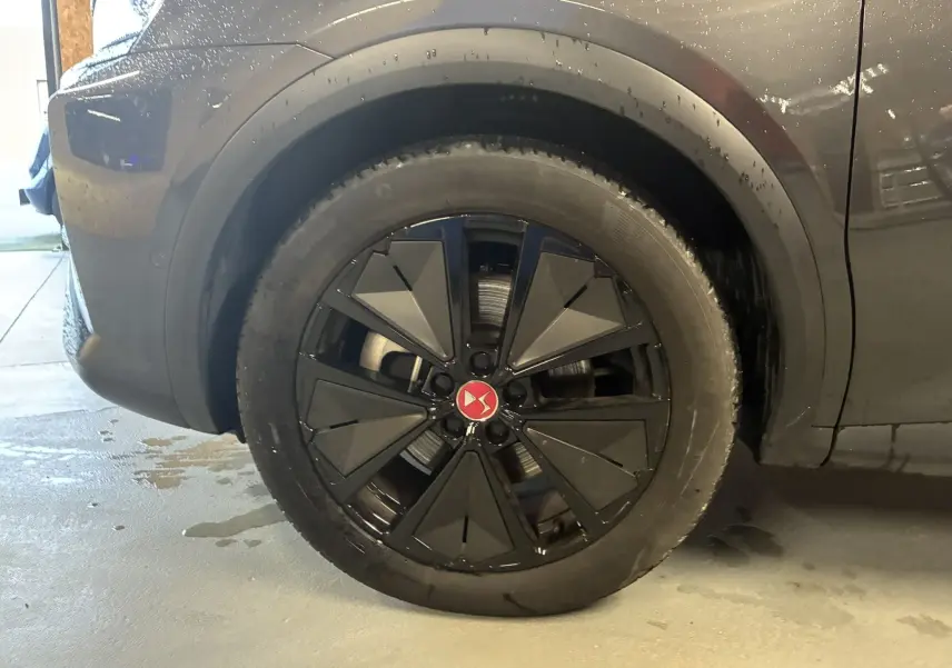 Gros plan sur la roue arrière droite noire avec jante stylisée du DS7 E-TENSE gris 2024, mettant en valeur le logo DS rouge central.