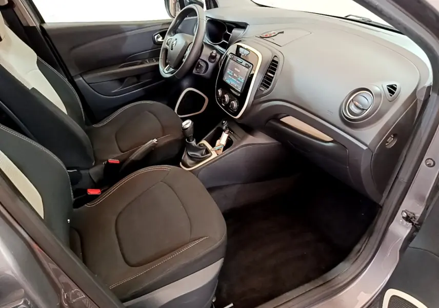 Vue intérieure côté conducteur du Renault Captur gris foncé, montrant le tableau de bord avec écran tactile et volant multifonctions cuir.