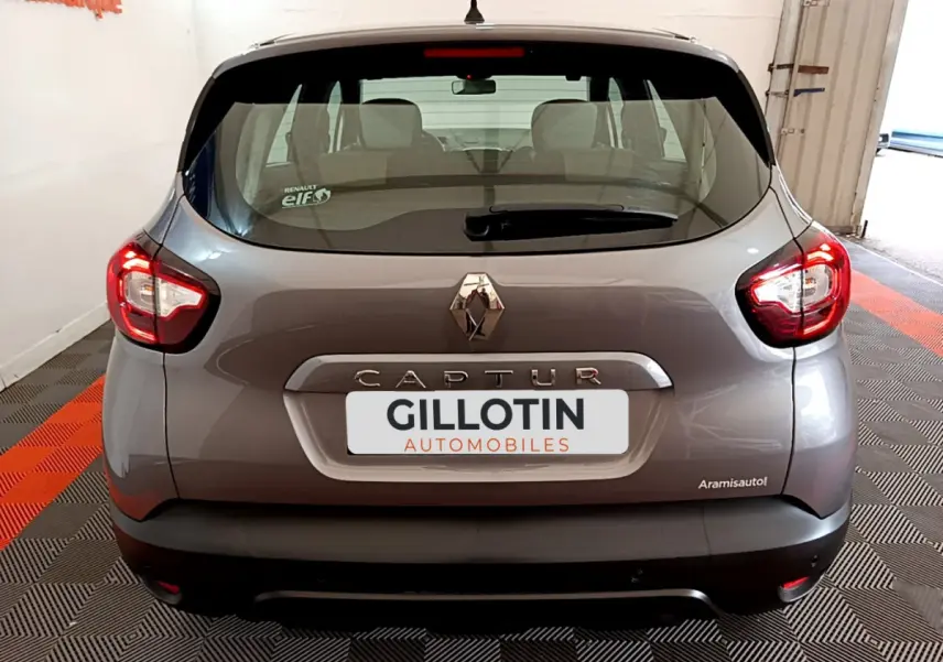 Vue arrière d'un Renault Captur gris foncé 2018 avec feux arrière allumés et logo Renault bien visible.