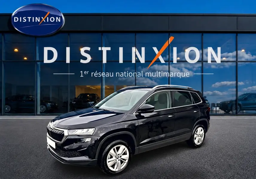 SKODA KAROQ noir 2025 en 3/4 avant droit, avec jantes alu et barres de toit visibles devant un showroom Distinxion.