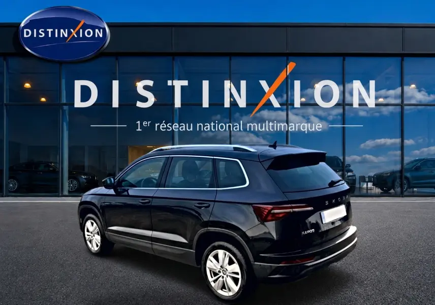 Vue 3/4 arrière droite d'un Skoda Karoq noir 2025 avec jantes alu, barres de toit et becquet arrière visible.