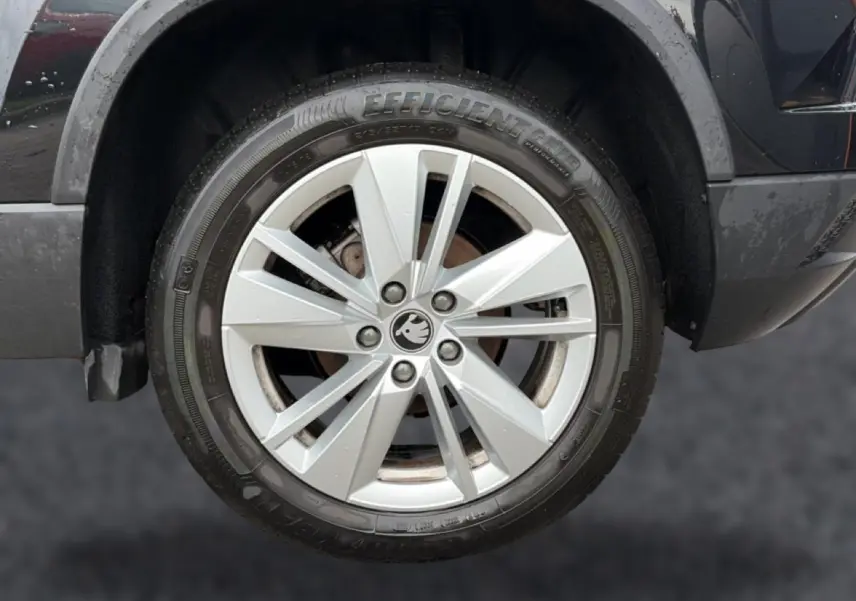 Gros plan sur la roue avant droite du Skoda Karoq noir, mettant en valeur la jante alu argentée et le logo central.