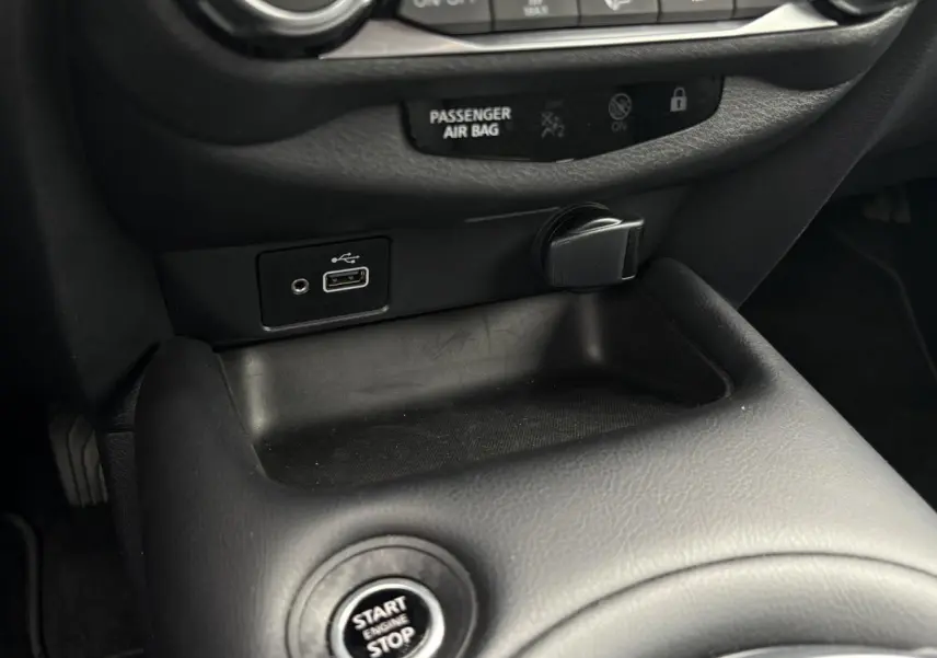 Gros plan sur la console centrale noire du Nissan Juke blanc perle, montrant le bouton Start/Stop et une prise USB.