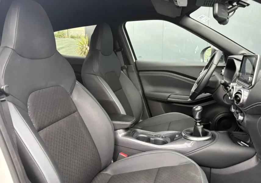 Intérieur du Nissan Juke 2024 vu côté conducteur, sièges noirs en TEP/tissu et levier de vitesse manuel visible.