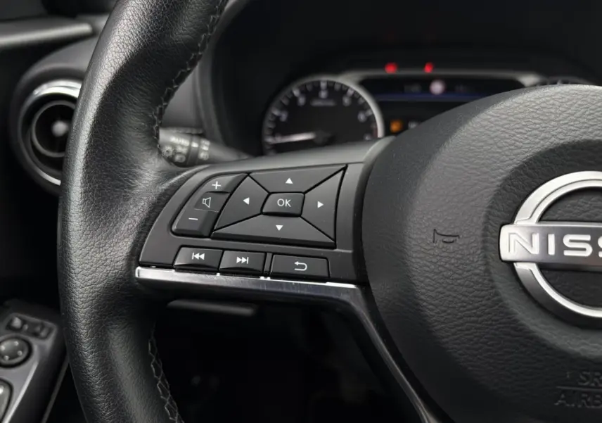 Gros plan sur le volant noir du Nissan Juke 2024, avec commandes multifonctions et logo Nissan au centre.