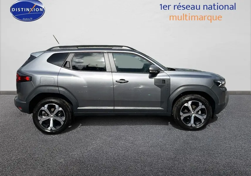 Profil droit du Dacia Duster 2025 gris schiste avec jantes alu et barres de toit visibles sur fond neutre.