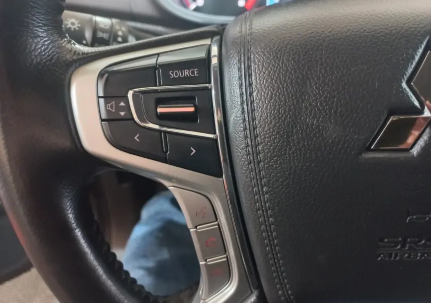 Gros plan sur le volant cuir noir du Mitsubishi L200 2020, avec commandes audio et téléphone intégrées à gauche.