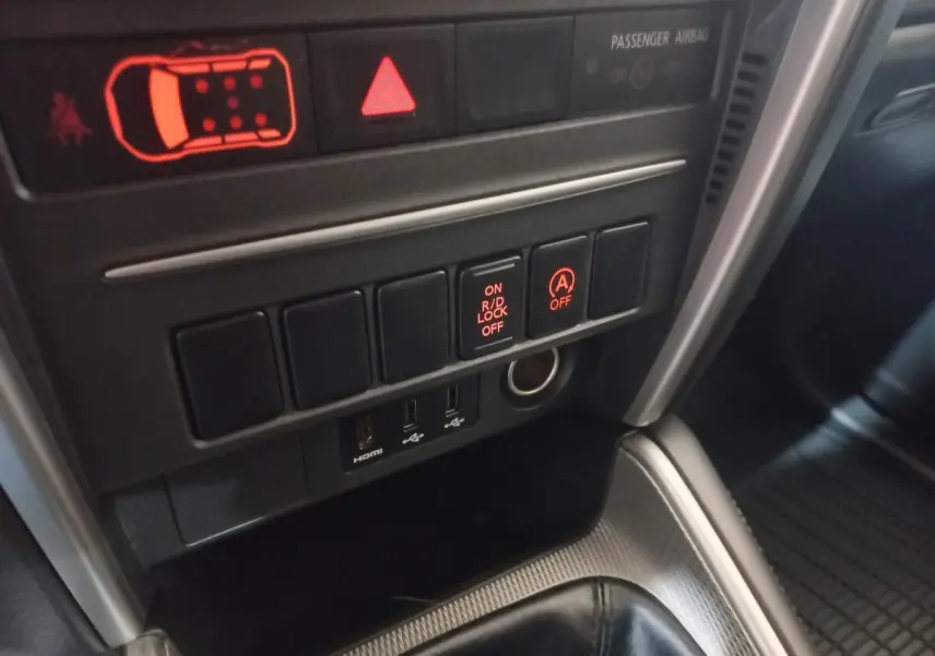 Gros plan sur les commandes centrales du Mitsubishi L200 2020, avec boutons lumineux et prises USB visibles.