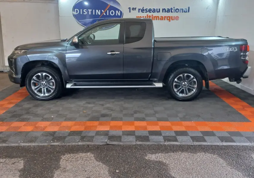 Vue de profil côté gauche d'un pick-up Mitsubishi L200 gris foncé avec jantes alliage et marquage 4x4 à l'arrière.