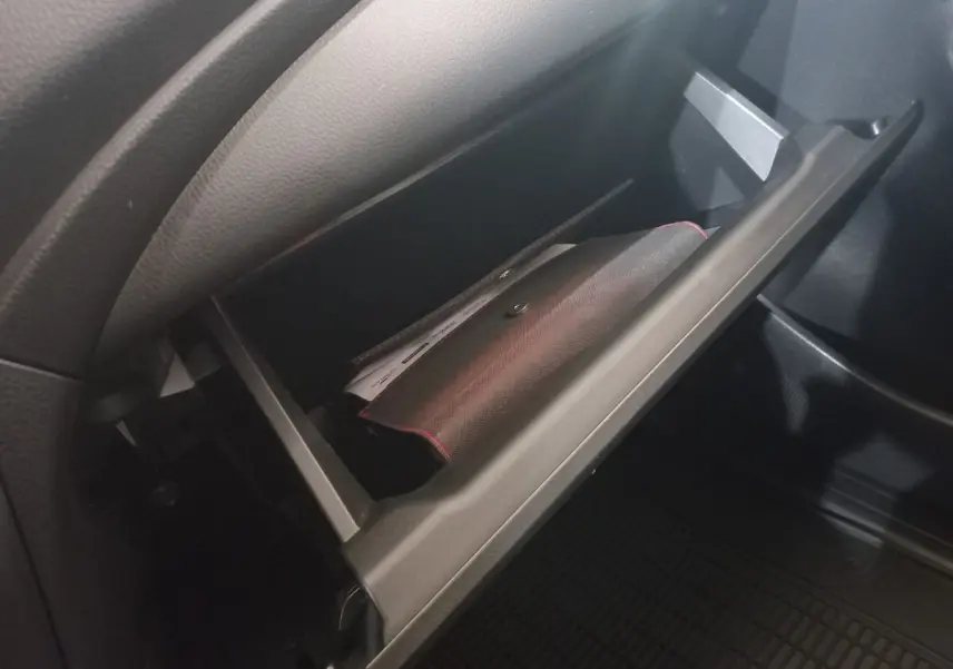 Gant de rangement ouvert côté passager intérieur du Mitsubishi L200 gris foncé, montrant un document à l'intérieur.