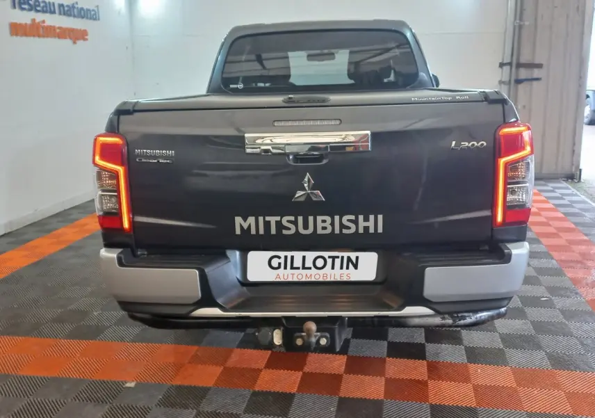 Vue arrière d’un pick-up Mitsubishi L200 gris foncé avec feux allumés et attelage visible en intérieur showroom.