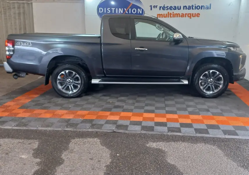 Vue de profil droit d’un pick-up Mitsubishi L200 gris foncé avec jantes alliage et marchepieds latéraux visibles.