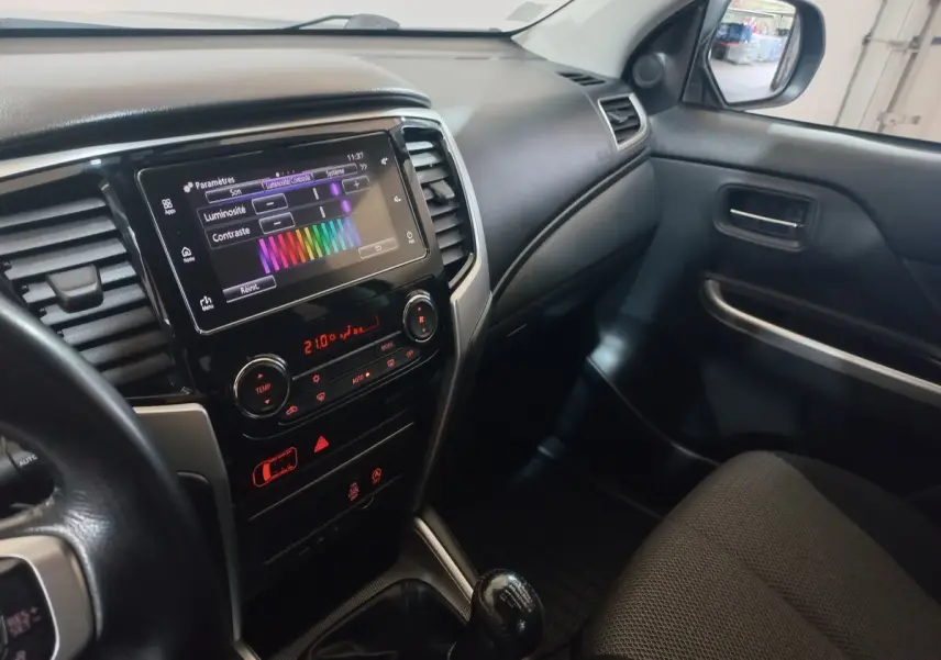 Vue intérieure côté passager du Mitsubishi L200 2020, tableau de bord noir avec écran tactile et levier de vitesses manuel.