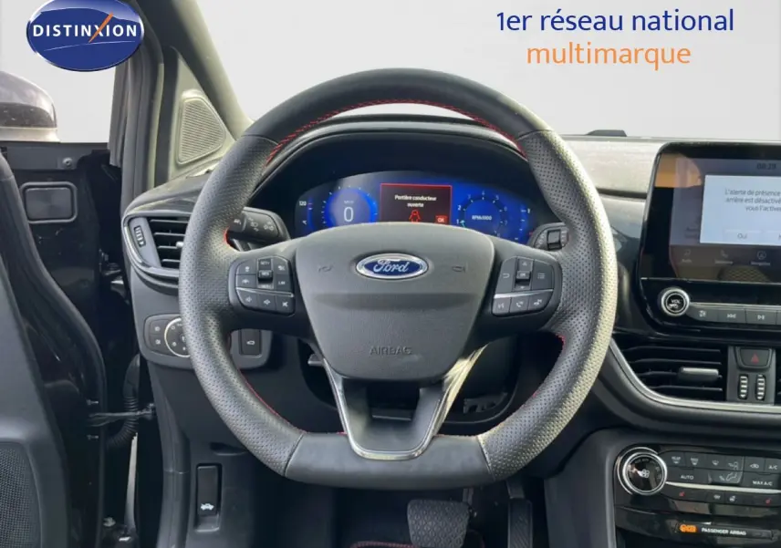 Vue intérieure centrée sur le volant perforé noir avec surpiqûres rouges du Ford Puma 2023, tableau de bord et écran tactile visibles.