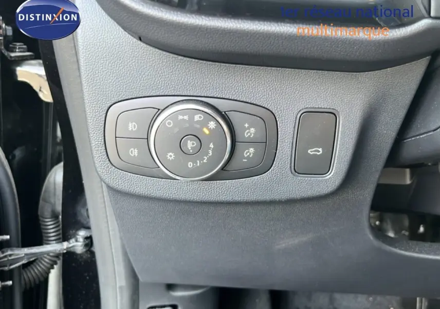Détail du tableau de bord côté gauche avec commandes d’éclairage et bouton d’ouverture du coffre sur Ford Puma noir Agate Metal 2023.