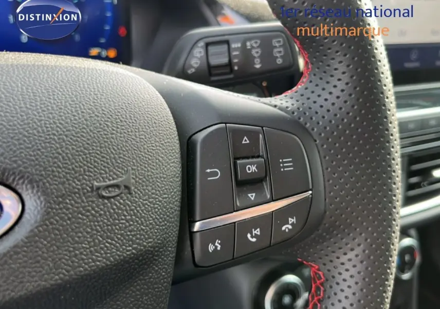 Gros plan sur le volant perforé avec surpiqûres rouges du Ford Puma noir agate, montrant les commandes multifonctions côté gauche.