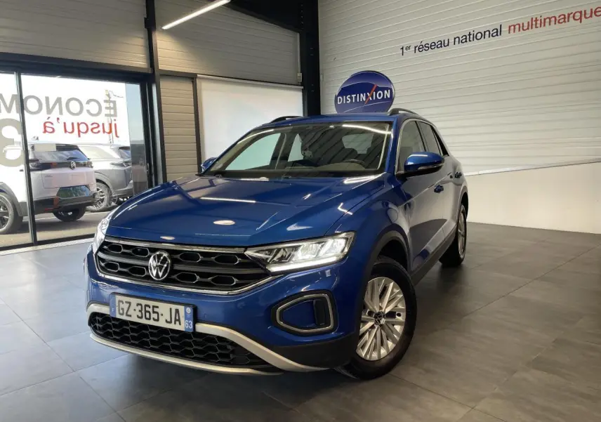 Volkswagen T-Roc bleu en 3/4 avant droit dans un showroom avec jantes alliage et calandre noire.