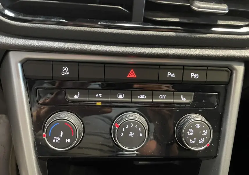 Gros plan sur la console centrale noire du Volkswagen T-Roc bleu, montrant les commandes de climatisation et d’alerte.