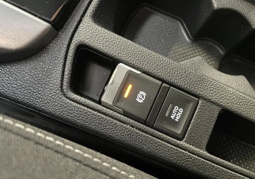 Gros plan sur le bouton de frein de stationnement électromécanique et fonction Auto Hold dans l'habitacle noir du Volkswagen T-Roc.