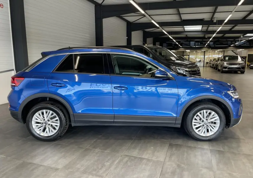 Vue latérale droite d'un Volkswagen T-Roc bleu 2022 en showroom avec jantes alliage et vitres teintées.