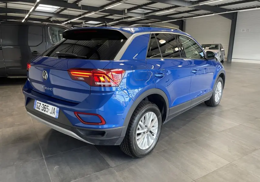 Vue 3/4 arrière droite d'un Volkswagen T-Roc bleu avec feux arrière LED allumés dans un garage.