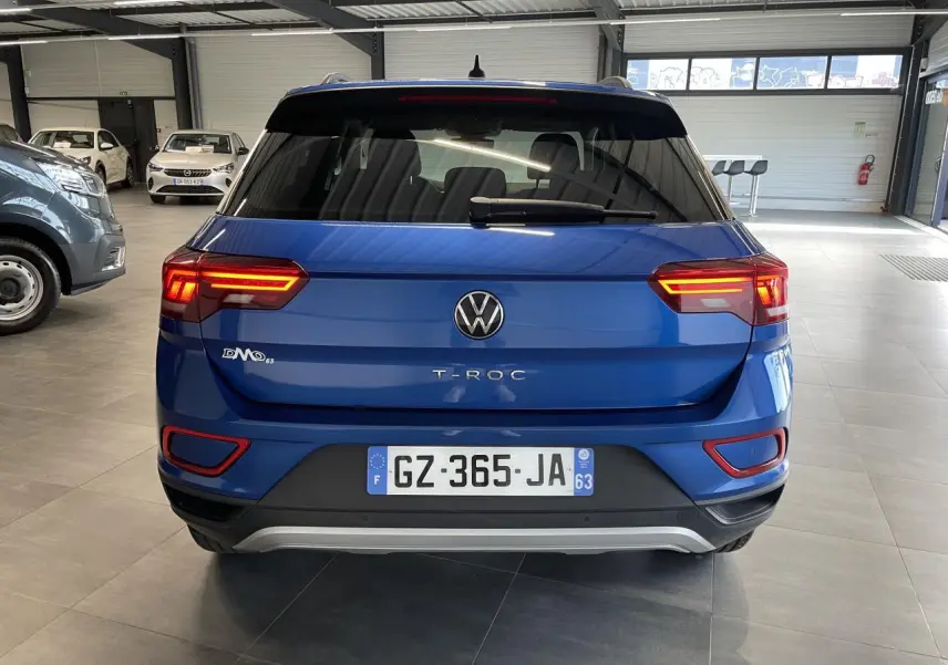 Vue arrière d'un Volkswagen T-Roc bleu 2022 avec feux LED allumés dans un showroom.