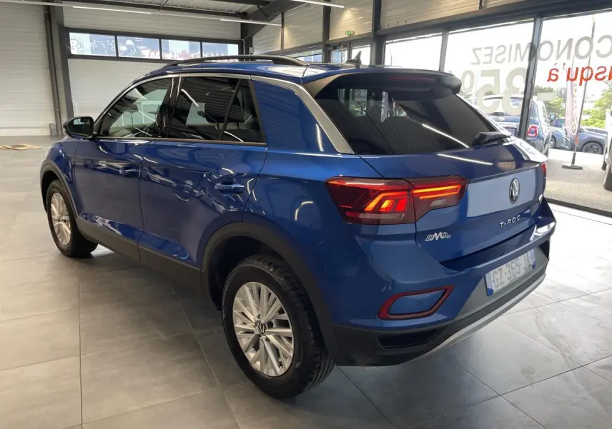 Vue 3/4 arrière droite d'un Volkswagen T-Roc bleu avec feux arrière allumés et jantes alliage en showroom.