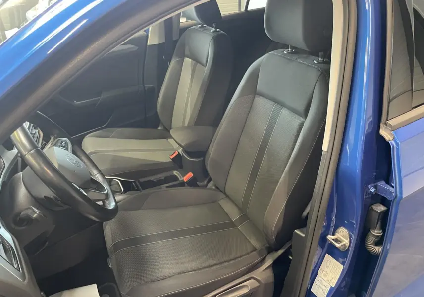 Vue intérieure côté conducteur du Volkswagen T-Roc bleu 2022, sièges tissu noir avec accoudoir central.