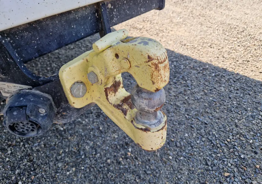 Gros plan sur l'attelage jaune rouillé à l'arrière d'un Renault Master blanc, avec prise électrique visible à gauche.