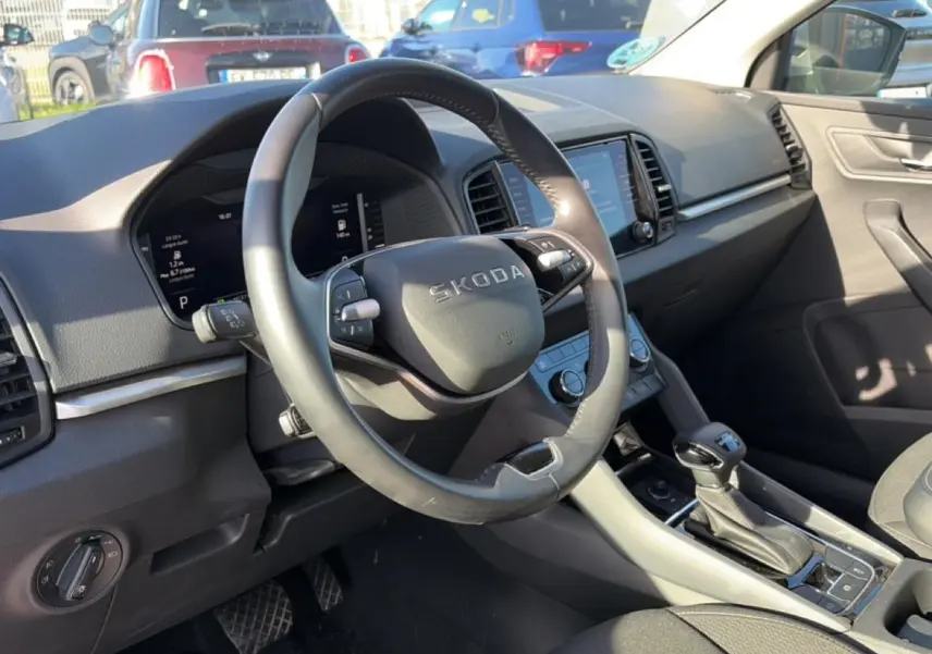 Vue intérieure côté conducteur du Skoda Karoq gris 2025, volant cuir multifonction et écran tactile central visible.