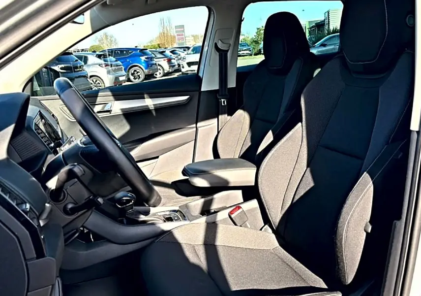 Vue intérieure côté conducteur du Skoda Karoq gris 2025, mettant en valeur les sièges avant et l'accoudoir central.