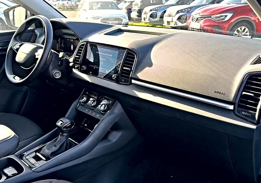 Intérieur avant droit du Skoda Karoq gris 2025, tableau de bord avec écran tactile et volant cuir multifonction.