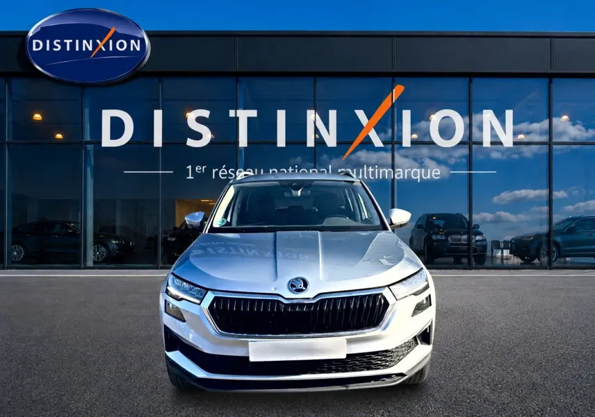 Vue frontale d'un Skoda Karoq gris 2025, avec calandre noire distinctive, devant une vitrine de concession multimarque.