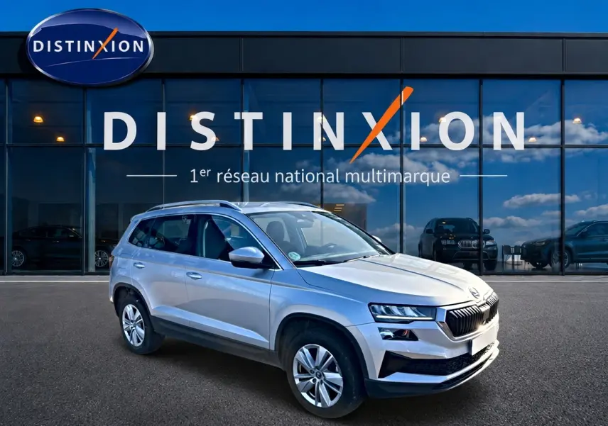 SKODA KAROQ gris 3/4 avant droit, SUV compact avec jantes alu et barres de toit devant vitrine Distinxion.