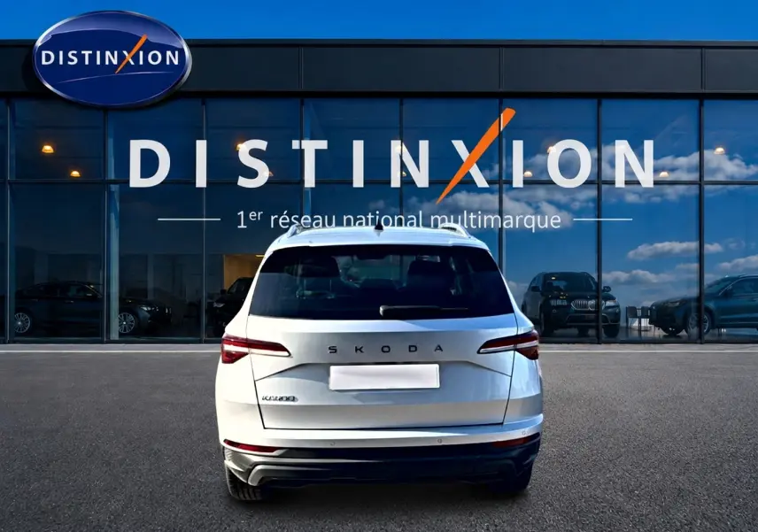 Vue arrière d'un Skoda Karoq gris 2025 garé devant une vitrine avec logo Distinxion en arrière-plan.