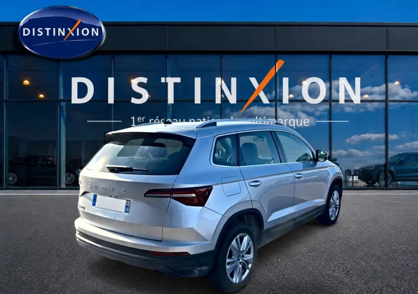 Vue 3/4 arrière droite d’un Skoda Karoq gris devant une vitrine avec logo Distinxion.